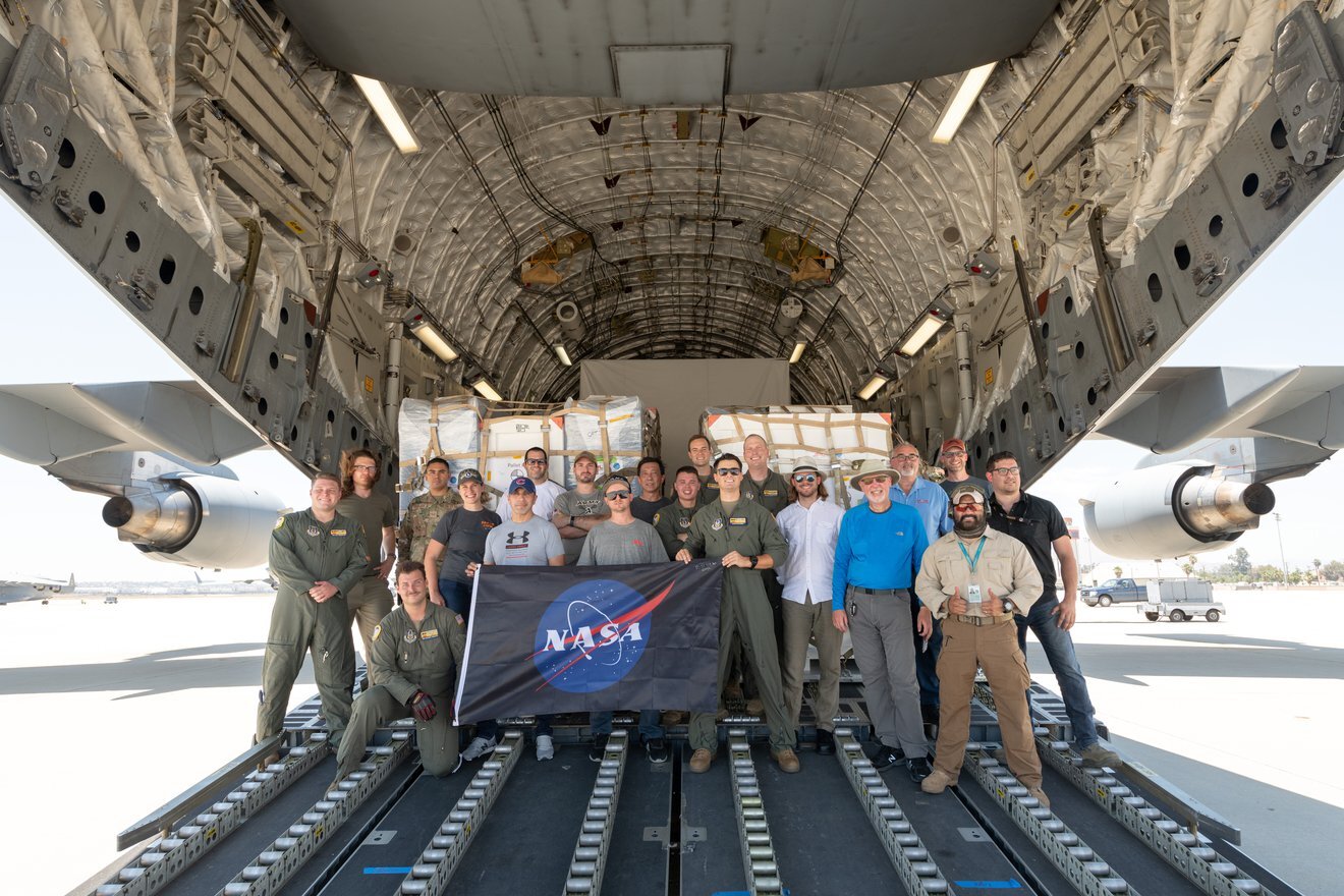 A photo of SWOT team members who helped load the mission's instruments in a plane, holding up a NASA flag.