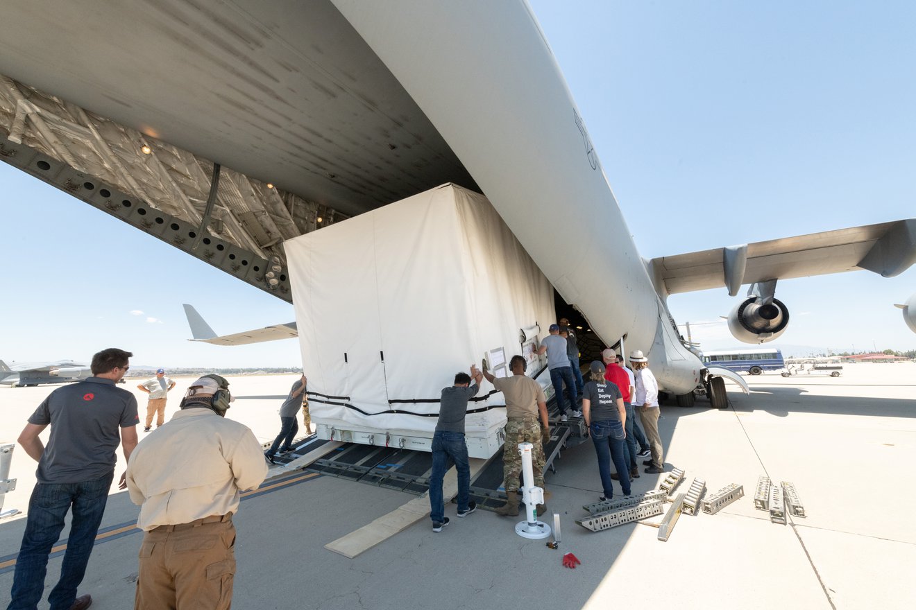 Team members pushing the SWOT scientific payload onto an airplane for transport to France.