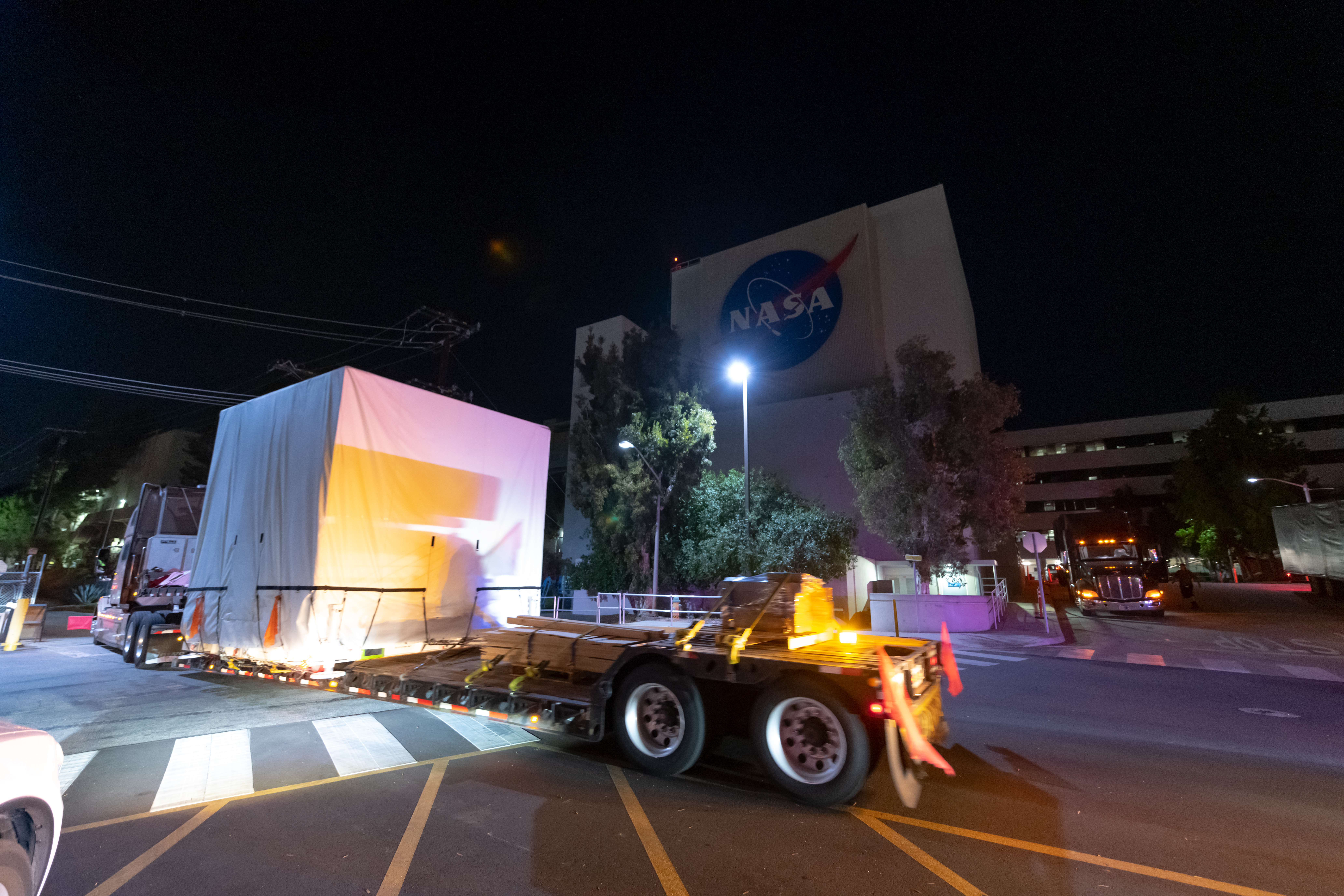A photo of the SWOT instrument  loaded on a truck outside of the Spacecraft Assembly Facility and the large NASA logo painted on it.